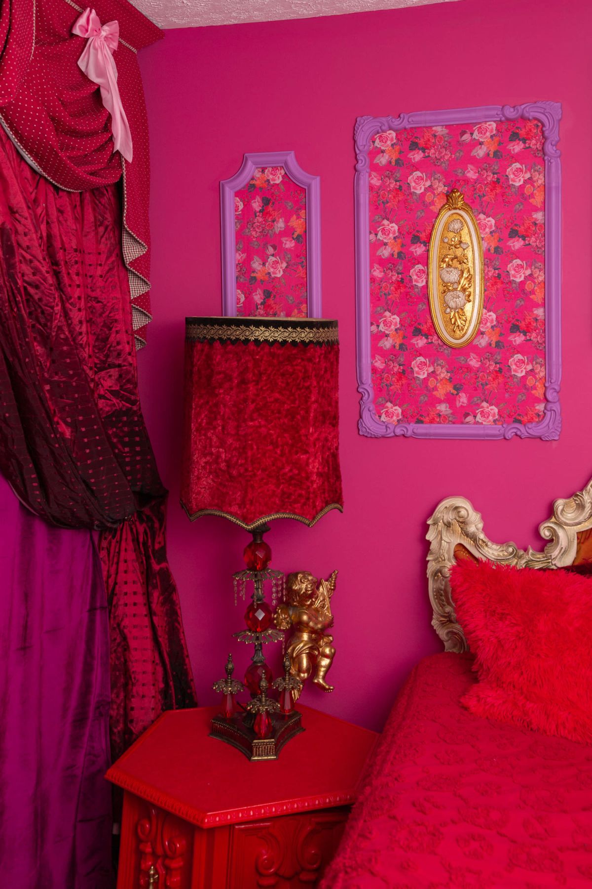 The image features a vibrant pink bedroom adorned with floral wallpaper, a decorative lamp, and a richly colored bedspread.